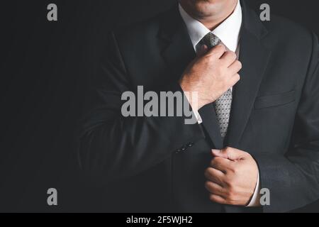uomo d'affari con abito nero che regola la sua cravatta su sfondo nero, pronto al lavoro concetto Foto Stock