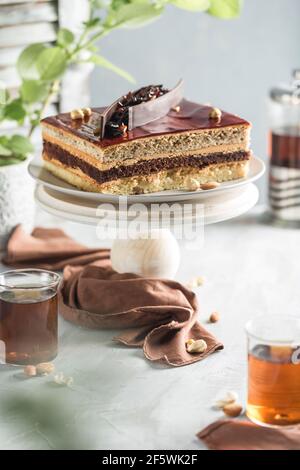 Torta al cioccolato con noci su un supporto in legno con una teiera e una tazza di tè su uno sfondo chiaro. Vista laterale con uno spazio per la copia del testo. Dessert per Foto Stock