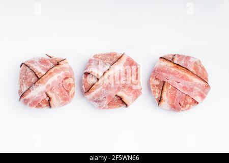 Primo piano di hamburger di pollo avvolti in nastri di pancetta. Semilavorato per uso domestico e gastro. Foto Stock