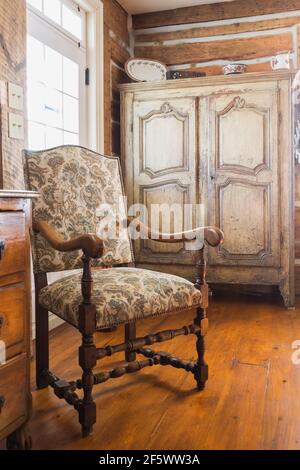 Louis XIII poltrona in legno rivestita in beige, marrone chiaro e motivi floreali di borgogna, latticello afflitto, armoire marrone in soggiorno all'interno della vecchia casa Foto Stock