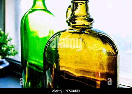 primo piano di bottiglie di colore giallo e verde vicino alla finestra Foto Stock