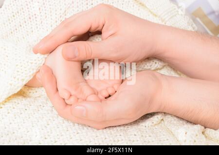 Piedi del bambino nelle mani maschili con sfondo morbido, primo piano. Messa a fuoco selettiva Foto Stock