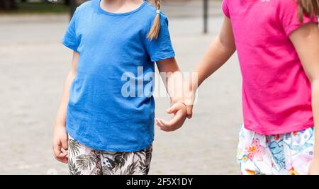 Due bambini anonimi in età scolastica, sorelle, fratelli insieme, una ragazza che afferra, prendendo altre ragazze mano, bambini che tengono le mani sulla strada. Famiglia, t Foto Stock