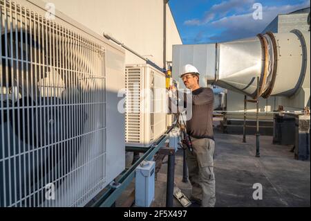 Tecnico HVAC che esegue la manutenzione di apparecchiature di climatizzazione commerciali sul tetto dell'edificio in alto Foto Stock