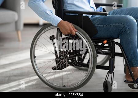 Vista ritagliata di un uomo nero per disabili seduto in sedia a rotelle a casa. Concetto di assistenza per disabilità e mobilità Foto Stock