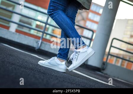 Donna con sneaker bianche in città. Gambe femminili che indossano jeans e scarpe sportive in pelle. Vita in città. Concetto di moda Foto Stock