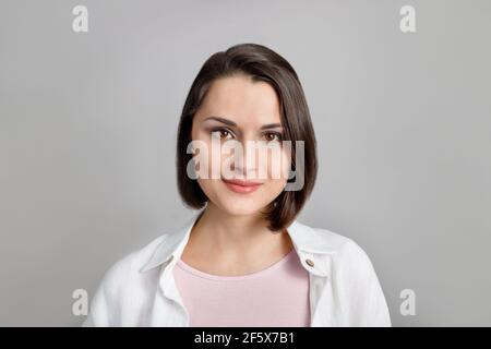 Alto ritratto chiave di giovane donna multietnica bruna sorridente in canotta rosa e camicia bianca guardando la macchina fotografica. Foto Stock