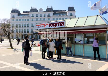 Giovani che si accaniscono per gelato indossando maschere per il viso su una primavera ventosa e soleggiata Domenica delle Palme Sardinero Santander Cantabria Spagna Foto Stock