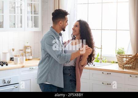 Amorevoli sposi arabi che ballano in interni di cucina e guardando L'uno con l'altro Foto Stock