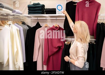 Vista posteriore della donna di vendita che lavora in un negozio di abbigliamento in piedi vicino alla rastrelliera con i vestiti e mettendo le cose in ordine Foto Stock