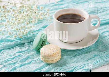 Tazza di caffè caldo e due amaretti su fondo di tessuto turchese. Colazione dolce con deliziosi biscotti alla meringa di mandorle. Macaroni colorati. Foto Stock
