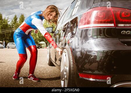 Mosca, Russia - 06 luglio 2020: Harley Quinn colpisce una macchina nera  parcheggiata con una mazza da baseball. C'è un'ammaccatura nella vettura,  la vettura è danneggiata. Cosplay, ragazza vestita come costume di