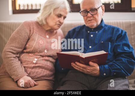 Coppie anziane che leggono la bibbia e pregano insieme a casa. Foto Stock