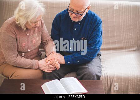 Coppie anziane che leggono la bibbia e pregano insieme a casa. Foto Stock