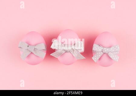 Uova di pasqua rosa con archi grigi in fila su sfondo rosa pastello, vista dall'alto. Foto Stock