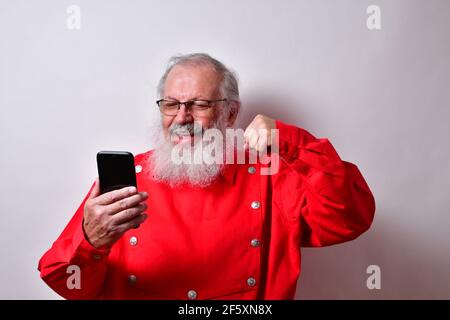 Uomo anziano in una camicia rossa con un elegante fedora hat ha successo usando il suo smartphone Foto Stock