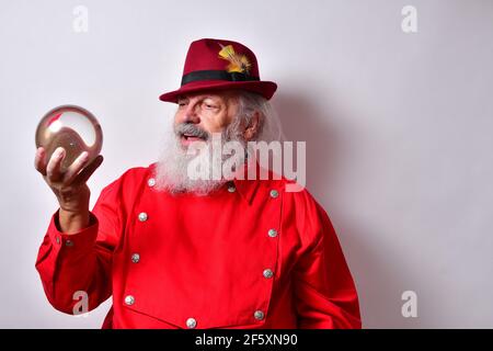 Vecchio maschio americano in una camicia rossa con un elegante cappello fedora che esamina con attenzione una palla di cristallo Foto Stock