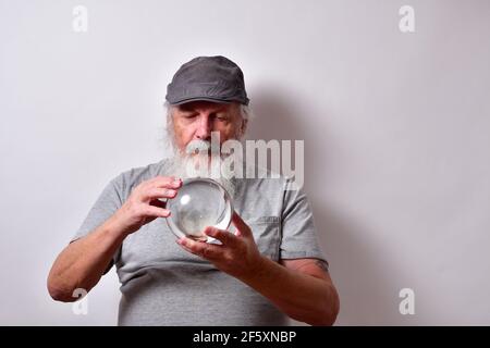 Vecchio maschio americano in una camicia grigia e grigio gatsby cappuccio che tiene una sfera di cristallo Foto Stock