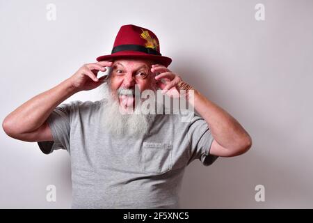 Vecchio maschio americano con camicia grigia e cappello rosso fedora fare una faccia pazzesca Foto Stock