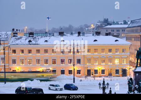 Helsinki, Finlandia - 13 gennaio 2021: Il tram si muove sulla piazza del Senato durante la forte tempesta di neve. L'edificio blu e' il Museo della Citta' di Helsinki Foto Stock