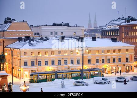 Helsinki, Finlandia - 13 gennaio 2021: Il tram si muove sulla piazza del Senato durante la forte tempesta di neve. L'edificio blu e' il Museo della Citta' di Helsinki Foto Stock