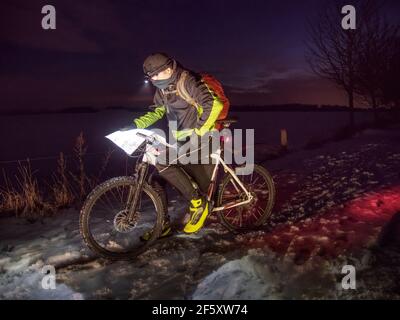 Lo sportivo si siede in mountain bike durante un viaggio serale sulla neve e risplende nell'itinerario di gara. Avventura invernale in bicicletta. Foto Stock