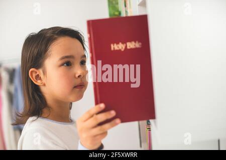 Poco prendendo la bibbia dalla sua biblioteca Foto Stock