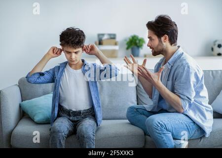 Violenza dei genitori. Arrabbiato papà scolding suo figlio innocente, che copre le orecchie per non ascoltare il padre arrabbiato Foto Stock