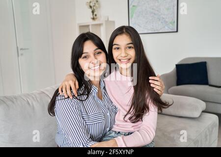 Felice adolescente figlia hugging giovane madre indiana a casa, ritratto. Foto Stock