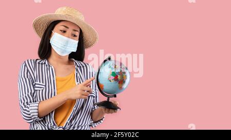 Sad Asian Tourist in Mask Holding Globe, che indica la mappa Foto Stock