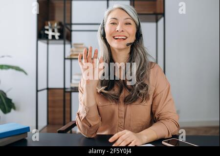Webcam headshot di bella riuscita sicuro maturo grigio-capelli asiatici, business lady, manager, avvocato, comunicare con il collega o il cliente in conferenza chiamata, guarda la fotocamera, saluto, sorrisi Foto Stock