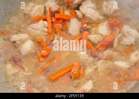 I pezzi di pollo vengono fritti con carote e cipolle rosse un calderone sulla griglia Foto Stock