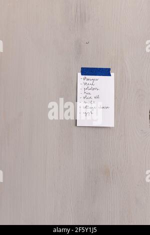 Lista della spesa scritta in una nota appiccicosa su sfondo di legno. Foto Stock