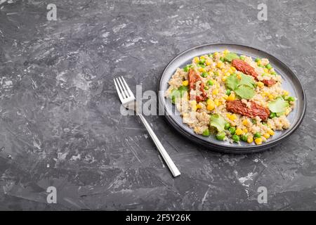 Porridge di quinoa con piselli verdi, mais e pomodori secchi su piastra di ceramica su fondo grigio di cemento. Vista laterale, primo piano, spazio di copia. Foto Stock
