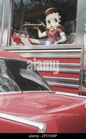 Betty Boop in piedi in vecchio stile anni '50 con finestra da pranzo auto classica rossa parcheggiata di fronte al ristorante o. inserire Foto Stock