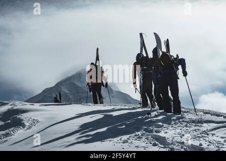 Vista posteriore di persone con zaini e splitboards su innevato montagna contro cielo nuvoloso Foto Stock