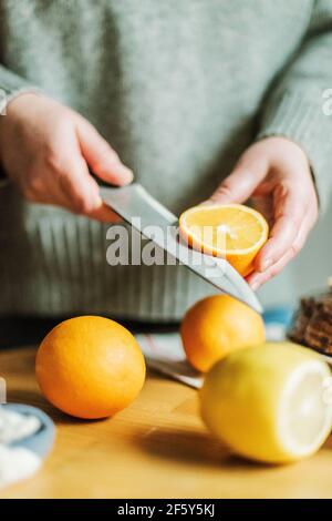 Donna anonima nella sua cucina a casa affettando arance con un sh Foto Stock