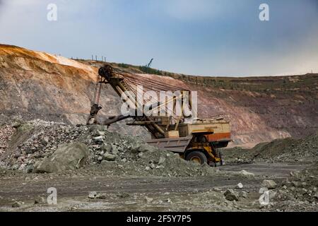 Rudny/Kazakhstan - Maggio 14 2012: Miniera a cielo aperto di minerale di ferro in cava. L'escavatore carica rocce nel dumper da cava Caterpillar. Foto Stock