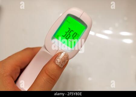 Closeup di una mano di donna che tiene una fronte digitale COVID-19 scanner di temperatura - termometro - con una normale temperatura del corpo umano, 36.5 gradi celsius. Foto Stock