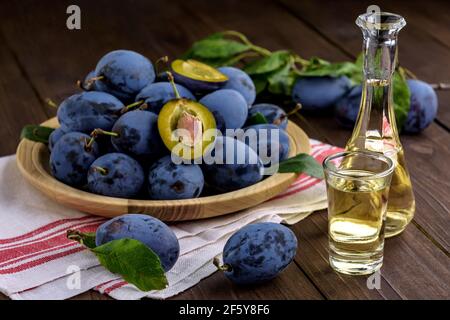 Brandy di prugne o schnapps in piccole bottiglie di vetro con prugne fresche e gustose su un tavolo di legno. Messa a fuoco selettiva. Foto Stock