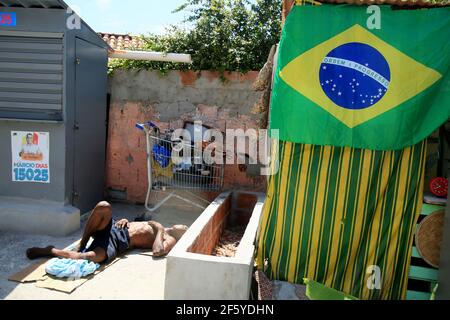 salvador, bahia, brasile - 21 gennaio 2021: L'uomo dorme sul pavimento accanto ad una bandiera brasiliana in una baracca nel quartiere di Itapua, nella città di Salv Foto Stock