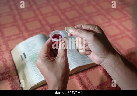 Uomo che tiene il pane e il vino nella comunione o Eucaristia. sacra bibbia a tavola sullo sfondo. Foto Stock