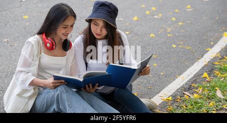 Due studenti felici che si siedono e si parlano in un campus del parco. Foto Stock