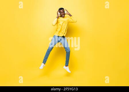 Felice giovane africano uomo che indossa le cuffie ascoltare la musica e. salto in giallo isolato studio sfondo Foto Stock