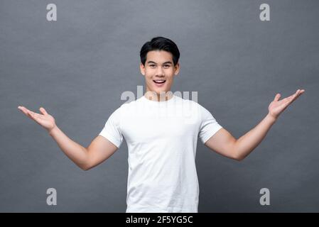 Sorprende sorridendo giovane asiatico che accoglie con cuore con le braccia aperte isolato su sfondo grigio dello studio Foto Stock