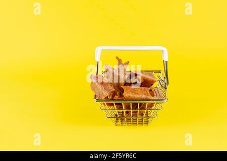 Cestino con le prelibatezze del cane su sfondo giallo. Dolcetti essiccati naturali per animali domestici. Pezzi di mammelle di vacca essiccate. Manzo a scatti per i cani. Supplemento per animali domestici Foto Stock