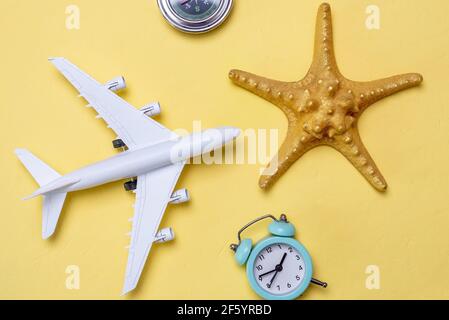 Miniatura di un aereo, una stella dorata e una bussola su sfondo giallo, vista dall'alto. Concetto di vacanze estive e viaggi in aereo Foto Stock