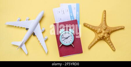 Miniatura di un aereo, biglietti aerei con passaporto e un orologio su sfondo giallo. Concetto di tempo per viaggiare. Foto Stock