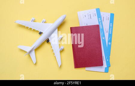 Miniatura dell'aereo, biglietti aerei e passaporto su sfondo giallo. Concetto di viaggio, vacanza e prenotazione di biglietti. Foto Stock