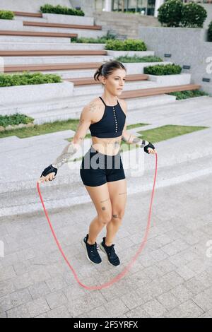 Bella giovane donna in forma che salta con la corda saltante all'aperto a. riscaldare prima dell'addestramento Foto Stock